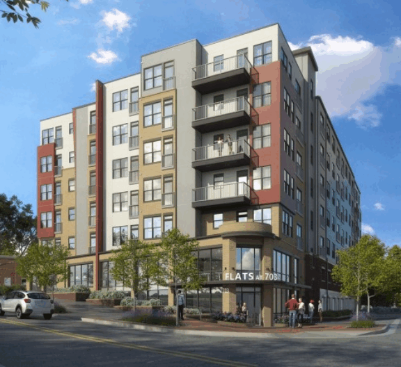 Modern multi-story apartment building with aluminum balcony railings and mixed exterior finishes under blue sky