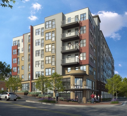 Modern multi-story apartment building with aluminum balcony railings and mixed exterior finishes under blue sky