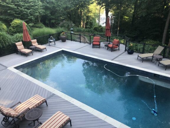 Glass panel aluminum railing around pool deck with gray composite decking