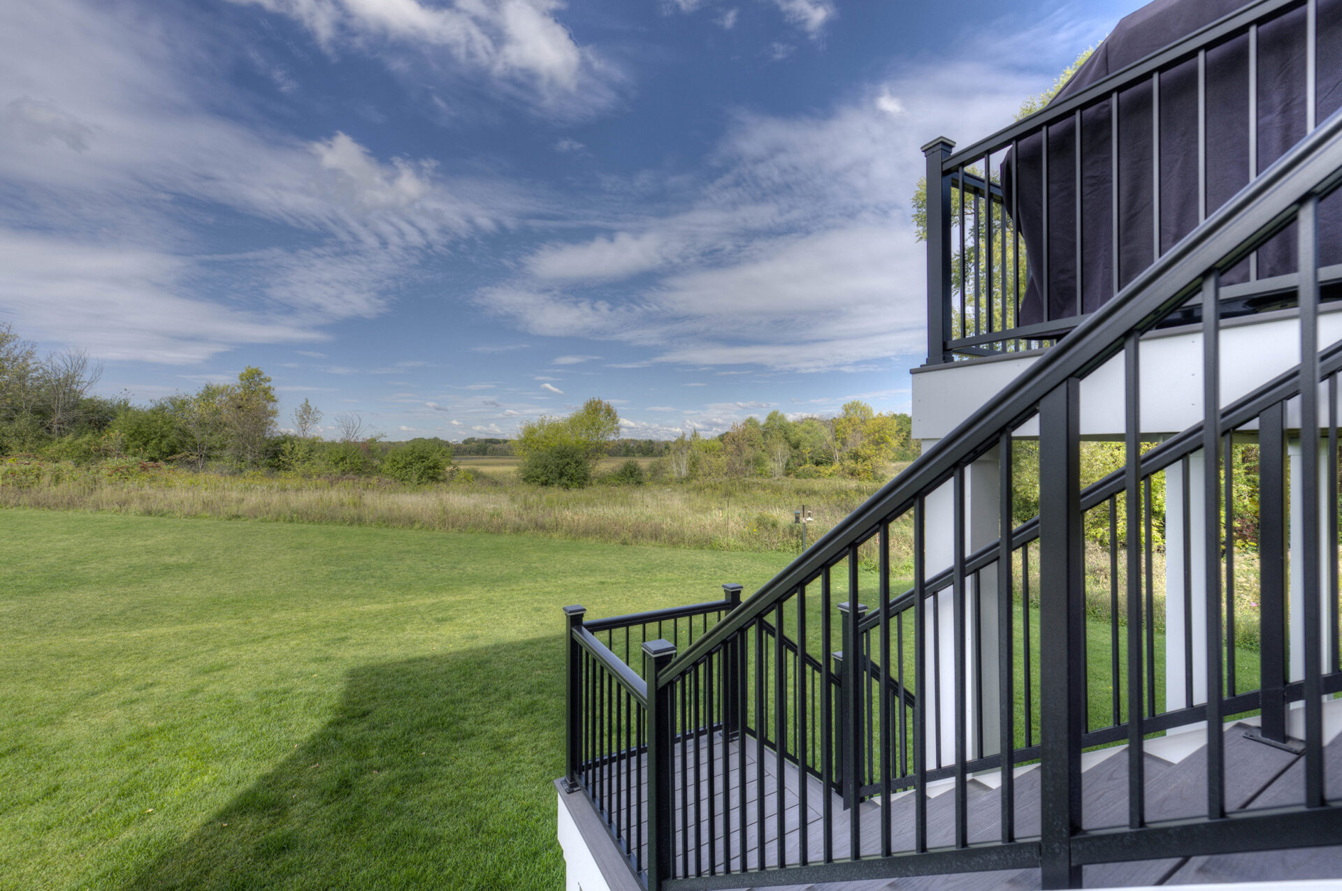 Black metal railing attached to a deck leading out to a lawn