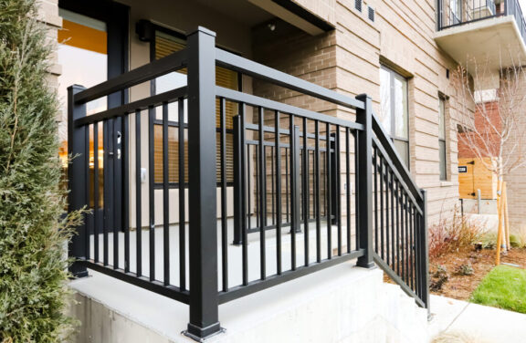 Black metal railing with vertical bars enclosing a small concrete porch at the entrance of a residential building
