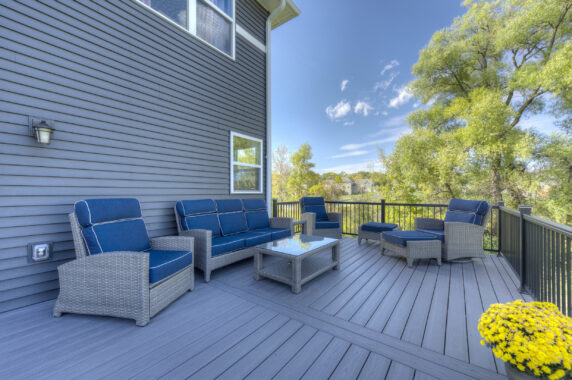 Black aluminum railing enclosing deck with gray wicker furniture and blue cushions under clear sky
