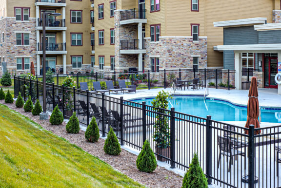 Black aluminum pool fence enclosing a clean swimming pool with lounge chairs and landscaped greenery