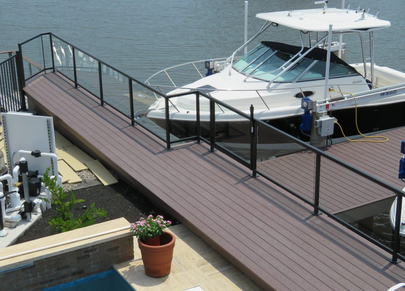 Black metal railing with clear glass panels on a waterfront dock by a white boat