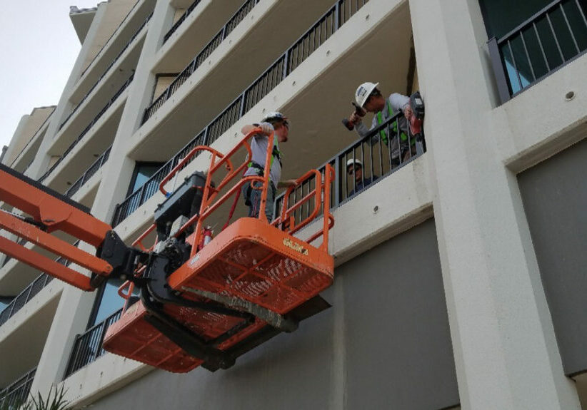 Construction workers installing powder-coated aluminum balcony railing using lift platform